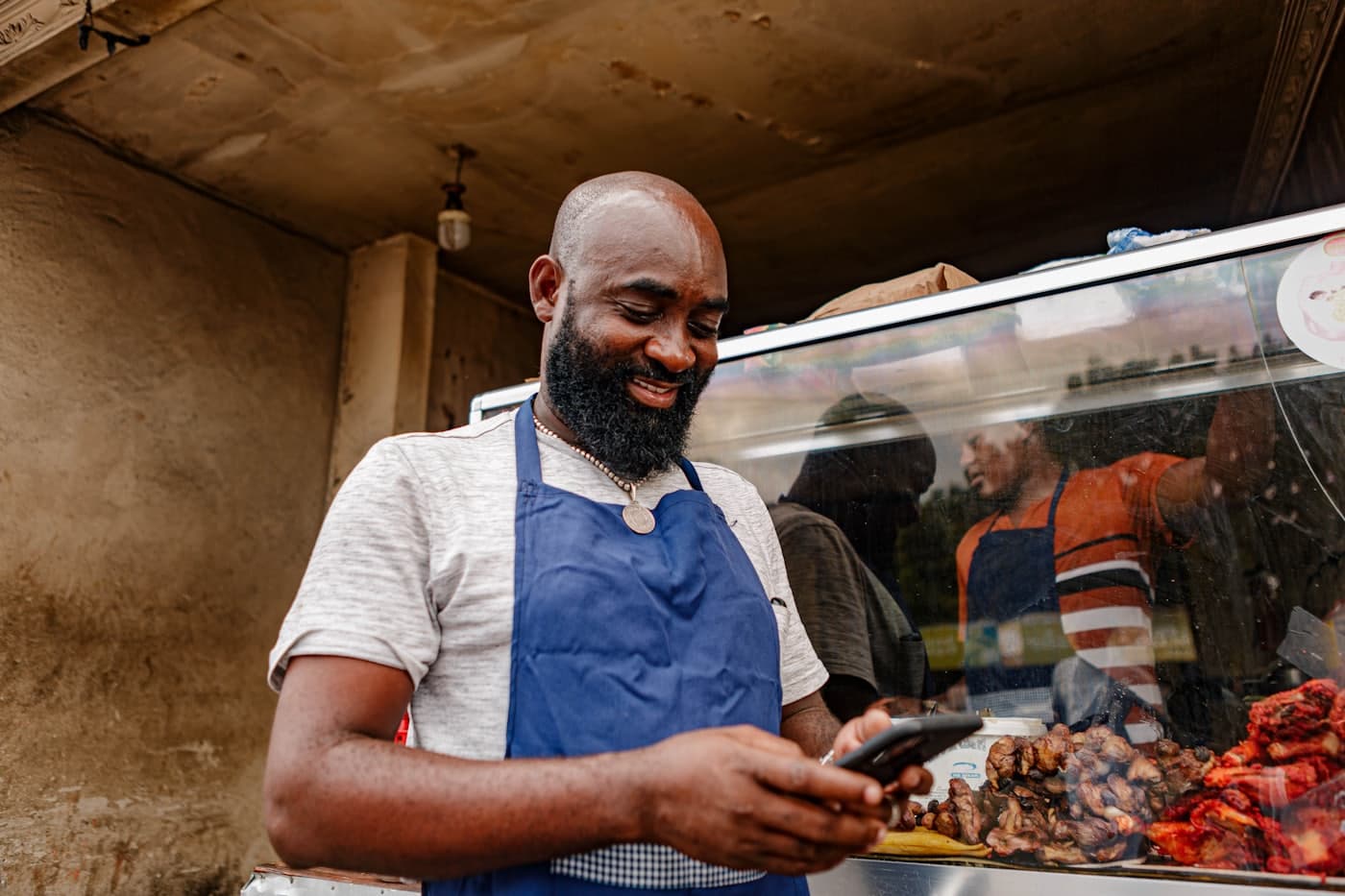 A food-stall owner in an apron checking his phone